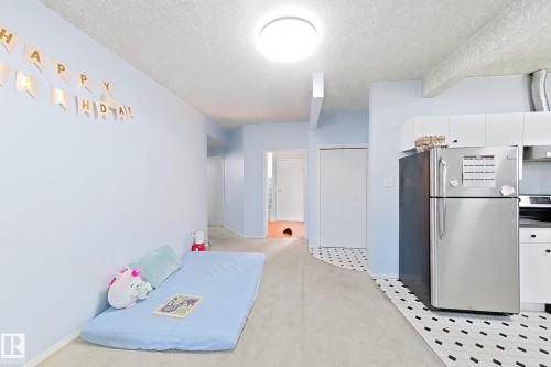 Open-concept living space featuring light-filled interiors with recessed ceiling lighting, stainless steel refrigerator, white cabinetry, and a geometric black-and-white tile floor throughout the kitchen and adjoining areas - 3015 37 Street Nw, Edmonton, AB 