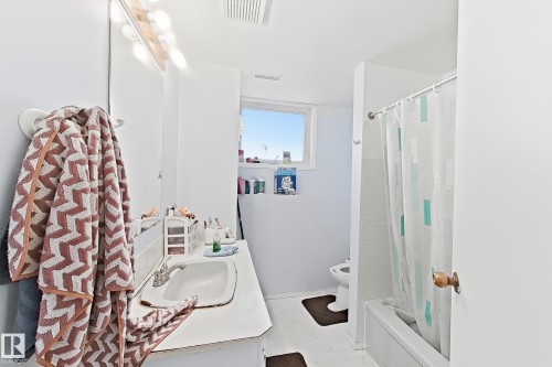Bright and spacious bathroom featuring clean white finishes, a pedestal sink with chrome faucet, recessed ceiling lighting, large mirror, and an enclosed shower/tub combination with glass enclosure and coordinating tile work - 3015 37 Street Nw, Edmonton, AB 