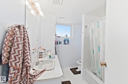 Bright and spacious bathroom featuring clean white finishes, a pedestal sink with chrome faucet, recessed ceiling lighting, large mirror, and an enclosed shower/tub combination with glass enclosure and coordinating tile work - 