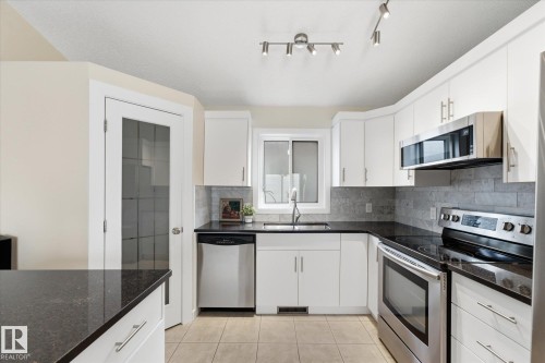 Kitchen featuring white cabinetry, dark countertops, a tile backsplash, and stainless steel appliances - 1709 Turvey Bend Bend Nw, Edmonton, AB 