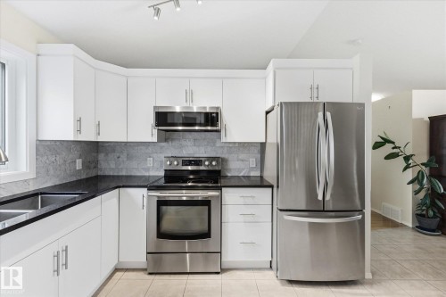 White cabinetry with brushed nickel hardware, stainless steel appliances, dark stone countertops, and a gray tile backsplash - 1709 Turvey Bend Bend Nw, Edmonton, AB 