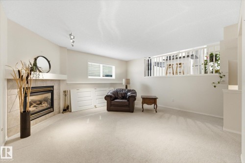 Carpeted flooring with a tiled fireplace surround, integrated storage cabinetry, and a window with blinds - 1709 Turvey Bend Bend Nw, Edmonton, AB 