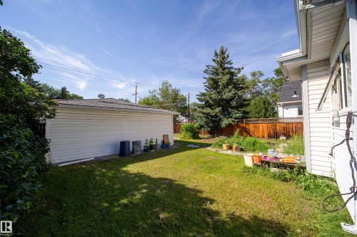 Expansive grass area with a detached garage featuring horizontal siding and a shingled roof, bordered by a wood fence - 10738 129 Street Nw, Edmonton, AB 