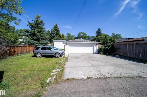 Detached garage with a roll-up door, paved driveway, and adjacent grassy area, bordered by a wood fence - 10738 129 Street Nw, Edmonton, AB 