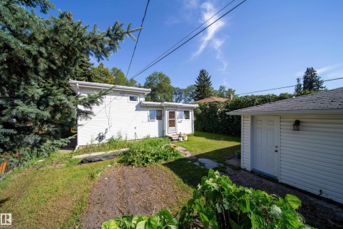 Rear exterior with white siding, detached garage, and mature landscaping - 10738 129 Street Nw, Edmonton, AB 