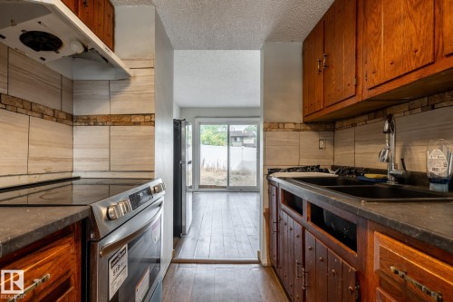 Kitchen featuring wood cabinetry, stone-finish countertops, ceramic tile backsplash, and stainless steel range - 54 Lakewood Village Nw, Edmonton, AB 