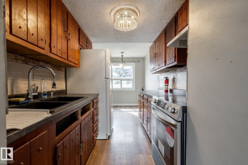 Galley kitchen featuring wood-finish cabinetry, a double basin sink, and a built-in range - 54 Lakewood Village Nw, Edmonton, AB 