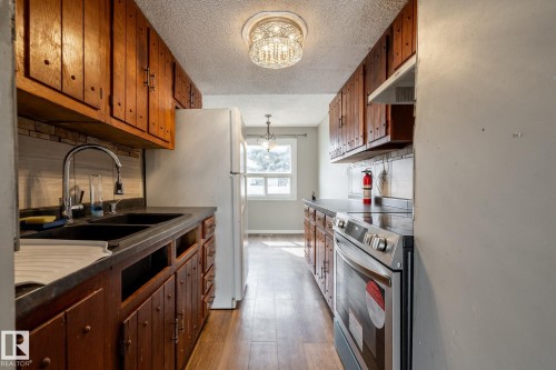 Wood-finish flooring, wood cabinetry, dual basin sink, integrated appliances, and a decorative ceiling light fixture - 54 Lakewood Village Nw, Edmonton, AB 