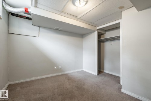 Carpeted room with a drop ceiling, featuring a built-in closet with shelving and a hanging rod - 54 Lakewood Village Nw, Edmonton, AB 
