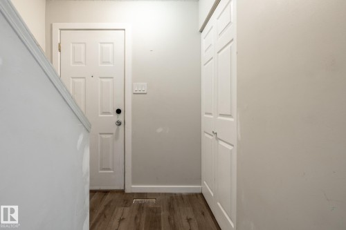 Wood-finish flooring with a white six-panel door, white bi-fold closet doors, and white walls - 54 Lakewood Village Nw, Edmonton, AB 