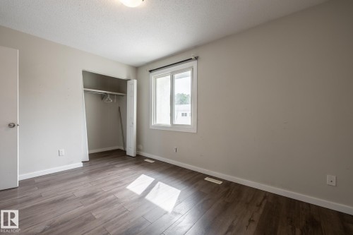 Wood-finish flooring, neutral wall tones, window with white trim, built-in closet with bi-fold doors, and a ceiling-mounted light fixture - 54 Lakewood Village Nw, Edmonton, AB 