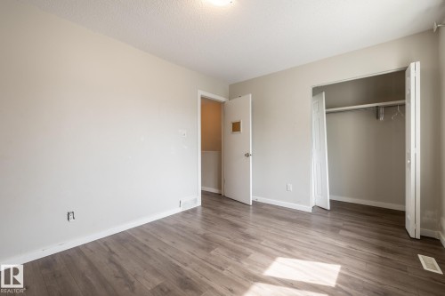 Neutral painted walls, wood-finish flooring, ceiling light fixture, and bifold closet doors with built-in shelving - 54 Lakewood Village Nw, Edmonton, AB 