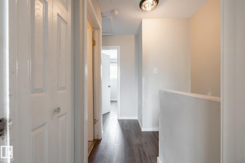 Hallway featuring wood-finish flooring, white paneled doors, and a flush mount ceiling light - 54 Lakewood Village Nw, Edmonton, AB 