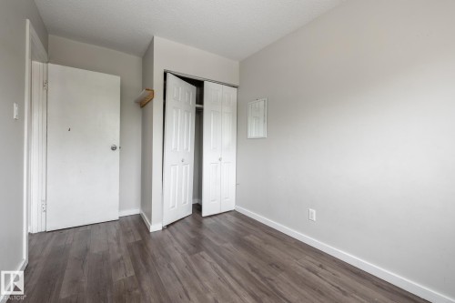 Wood-finish flooring with a neutral wall color, featuring a bi-fold closet door and a white paneled door - 54 Lakewood Village Nw, Edmonton, AB 