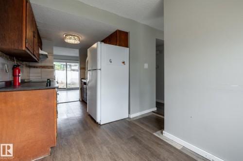Kitchen featuring wood-finish flooring, wood cabinetry, a tile backsplash, and a sliding glass door - 54 Lakewood Village Nw, Edmonton, AB 