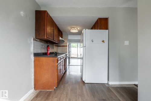 Kitchen featuring wood-finish flooring, dark wood cabinetry, dark countertops, and a tiled backsplash - 54 Lakewood Village Nw, Edmonton, AB 