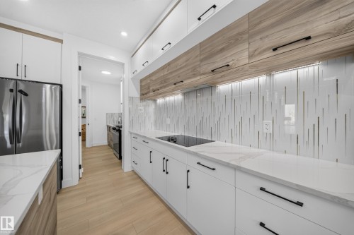 White and wood-finish cabinetry with black hardware, white countertops, stainless steel appliances, and wood-finish flooring - 17128 2 Street Nw, Edmonton, AB 