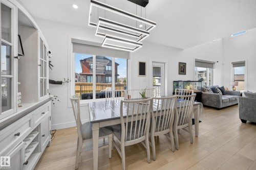 Open-concept living area featuring light wood-finish flooring, a modern linear chandelier, and a built-in hutch with glass-front cabinets - 17128 2 Street Nw, Edmonton, AB 