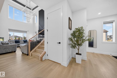 Vaulted ceilings with an expansive window arrangement, wood-finish flooring, staircase with wood treads and black metal spindles, contemporary chandelier, and a white interior door with matte black hardware - 17128 2 Street Nw, Edmonton, AB 