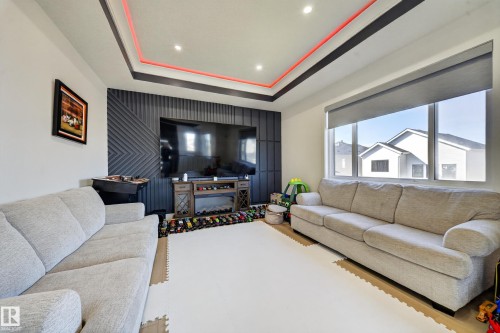 Recessed lighting with a tray ceiling, large picture window with roller shade, and feature wall with decorative paneling and electric fireplace - 17128 2 Street Nw, Edmonton, AB 