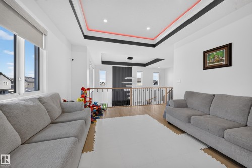 Recessed lighting, layered ceiling design with accent lighting, wood-finish flooring, white walls, and a wrought iron and wood banister - 17128 2 Street Nw, Edmonton, AB 
