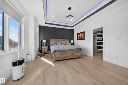 Light wood-finish flooring, accent wall with geometric paneling, indented ceiling with recessed lighting, modern ceiling light fixture, built-in closet shelving - 17128 2 Street Nw, Edmonton, AB 
