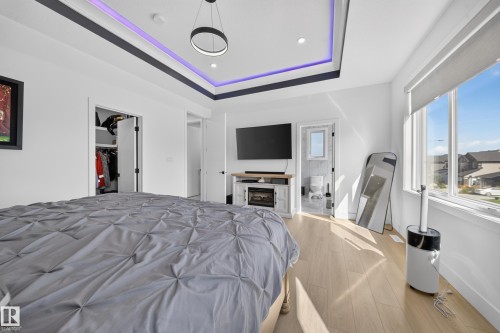Tray ceiling with perimeter lighting, recessed lighting, wood-finish flooring, built-in fireplace, and large window with roller shade - 17128 2 Street Nw, Edmonton, AB 