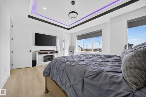 Recessed ceiling with perimeter lighting, large windows with roller shades, light wood-finish flooring, and a built-in electric fireplace console - 17128 2 Street Nw, Edmonton, AB 