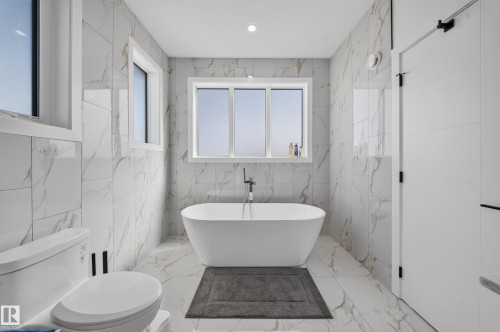 Freestanding soaking tub with a floor-mounted faucet, complemented by large format tile flooring and walls - 17128 2 Street Nw, Edmonton, AB 