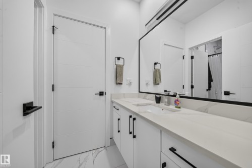 Vanity with integrated sink and stone countertop, white cabinetry with black hardware, large wall-mounted mirror, and tile flooring - 17128 2 Street Nw, Edmonton, AB 