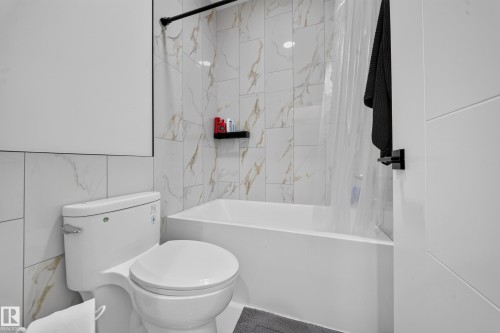 White subway tile surrounds the toilet and bathtub, complemented by a black shower rod and a black towel bar - 17128 2 Street Nw, Edmonton, AB 