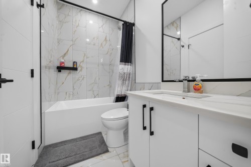 Bathroom featuring a built-in bathtub, a white vanity with an integrated sink, a large wall-mounted mirror, and wall-mounted tile - 17128 2 Street Nw, Edmonton, AB 