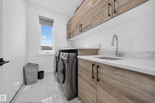 White walls, wood-finish cabinetry, white countertops, built-in sink, and a modern faucet - 17128 2 Street Nw, Edmonton, AB 