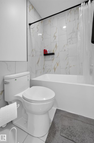 White ceramic toilet with a concealed trapway, integrated bathtub, and white and gold-veined tile surround - 17128 2 Street Nw, Edmonton, AB 