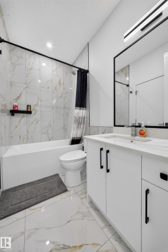 Contemporary bathroom featuring a white vanity with black hardware, an integrated sink, a rectangular framed mirror, and a tub with tiled surround - 17128 2 Street Nw, Edmonton, AB 