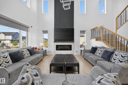 Double-height ceilings, wood-finish flooring, built-in fireplace, staircase with wood banister and metal spindles, and high window placements - 17128 2 Street Nw, Edmonton, AB 