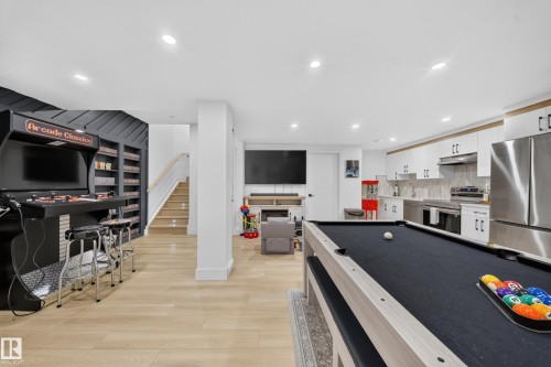 Spacious basement featuring wood-finish flooring, built-in shelving, a full kitchen with stainless steel appliances, and recessed lighting - 17128 2 Street Nw, Edmonton, AB 