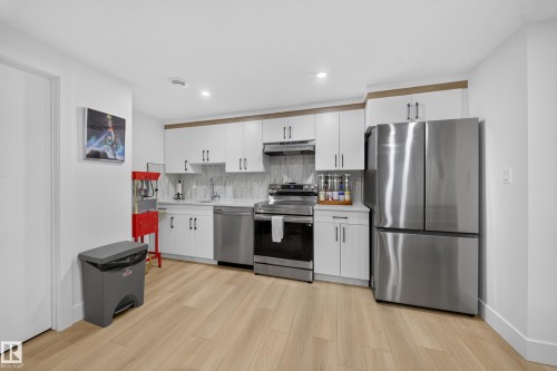 Contemporary basement kitchen with wood-finish flooring, white cabinetry, stainless steel appliances, and a tile backsplash - 17128 2 Street Nw, Edmonton, AB 