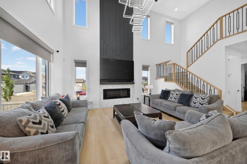 Two-story living area with high ceilings, light wood-finish flooring, and a contemporary fireplace with a tile surround - 17128 2 Street Nw, Edmonton, AB 