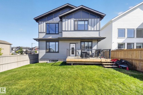 Two-story residence featuring light gray siding with dark gray vertical accents, a wood deck with black metal railings, and a green lawn - 17128 2 Street Nw, Edmonton, AB 
