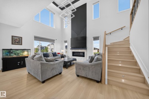 Vaulted ceilings, a contemporary fireplace with a fluted accent wall, light wood-finish flooring, a modern chandelier, and a wood staircase with integrated lighting - 17128 2 Street Nw, Edmonton, AB 