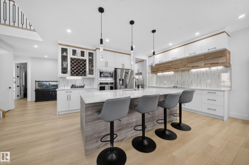 Expansive kitchen island with seating, integrated stainless steel appliances, white and wood-finish cabinetry, and a full-height backsplash - 17128 2 Street Nw, Edmonton, AB 