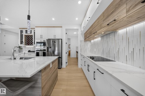 Contemporary kitchen featuring white cabinetry, wood-finish accents, and stainless steel appliances - 17128 2 Street Nw, Edmonton, AB 
