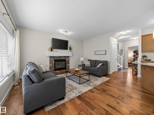 Living area featuring wood-finish flooring, a stone-faced fireplace with a white mantel, and track lighting - 6504 48 Avenue, Beaumont, AB - Indoor Photo Showing Living Room With Fireplace