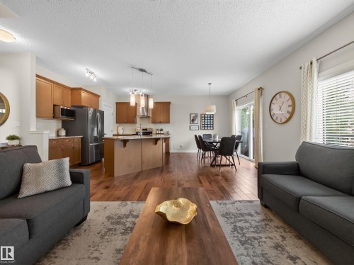 Spacious open-concept living area featuring wood-finish flooring, a kitchen island with seating, a dining area with pendant lighting, and a sliding glass door providing exterior access - 6504 48 Avenue, Beaumont, AB - Indoor Photo Showing Living Room