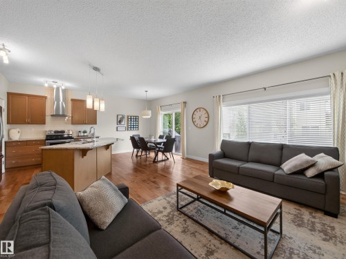 Open-concept living space featuring wood-finish flooring, a kitchen island with stone countertop, stainless steel appliances, and a dining area with direct outdoor access - 6504 48 Avenue, Beaumont, AB - Indoor Photo Showing Living Room