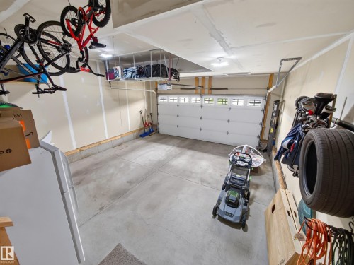 Spacious two-car garage featuring a sectional overhead door with upper window panels, overhead storage racks, and multiple ceiling-mounted light fixtures - 6504 48 Avenue, Beaumont, AB - Indoor Photo Showing Garage