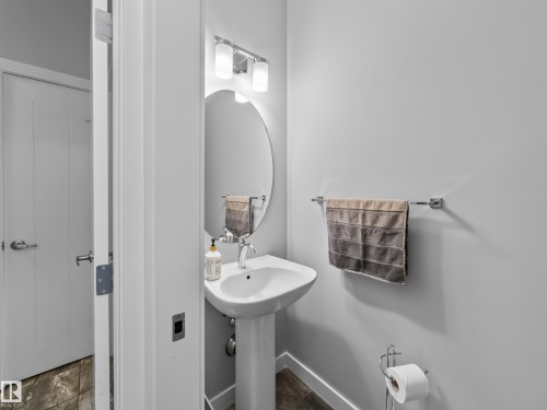 Pedestal sink with chrome faucet, complemented by an oval mirror and a three-light vanity fixture - 6504 48 Avenue, Beaumont, AB - Indoor Photo Showing Bathroom