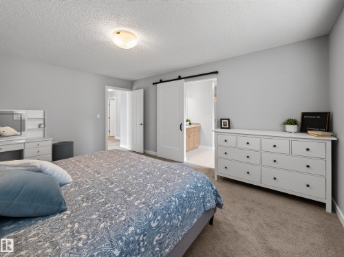 Carpeted bedroom featuring light gray walls, a ceiling-mounted light fixture, and a white barn door leading to an en-suite bathroom with a wood vanity - 6504 48 Avenue, Beaumont, AB - Indoor Photo Showing Bedroom