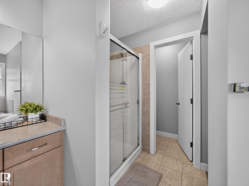 Bathroom featuring a glass-enclosed shower with tiled surround, light wood-finish vanity with countertop, large wall-mounted mirror, and tile flooring - 6504 48 Avenue, Beaumont, AB - Indoor